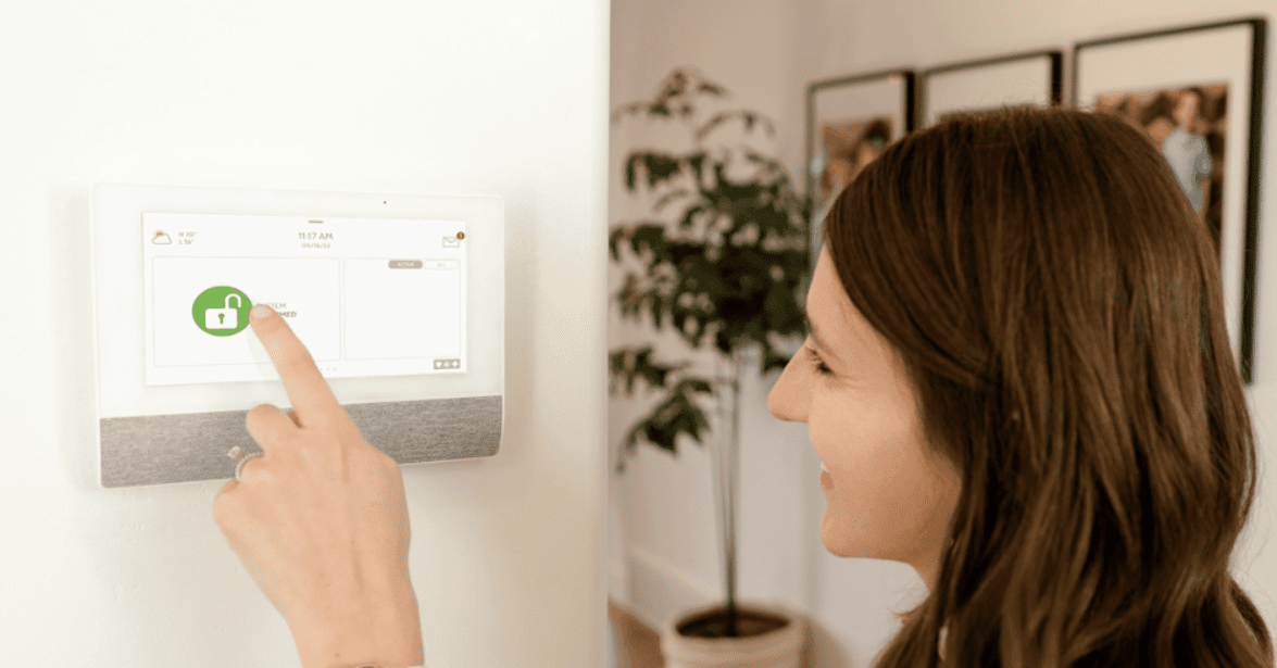 A smiling woman using a touchscreen home security system to arm and disarm her alarm, highlighting the ease of use and convenience of modern security systems