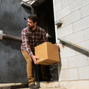 A man carrying a box exits a warehouse through a back door, representing employee theft and unauthorized inventory removal.
