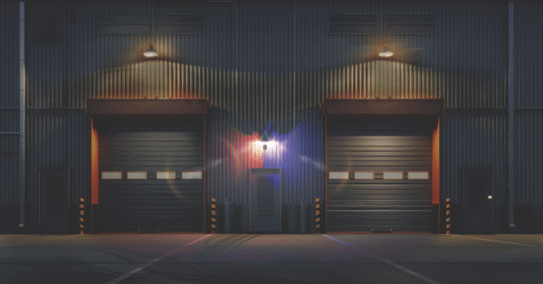 Exterior view of an industrial facility at night with bright security lighting above doors to deter intrusions.