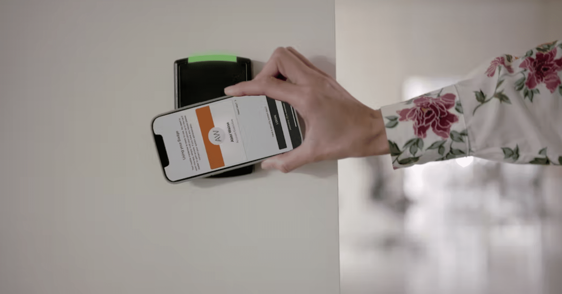 Person using mobile credentials on a smartphone to access a secure door through an access control system, holding the phone against a wall-mounted reader.